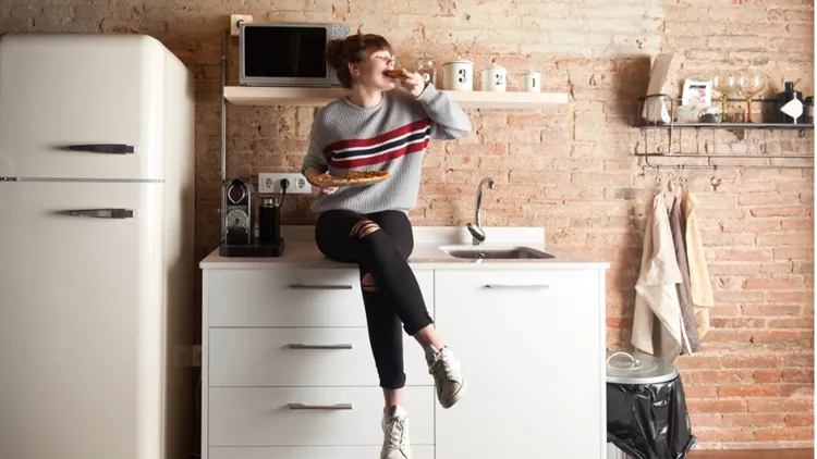 beautiful-girl-eating-pizza-in-a-modern-kitchen-picture-id910844022