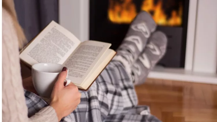 girl-in-front-of-the-fireplace-reading-book-and-warming-feet-on-fire-picture-id1060710610