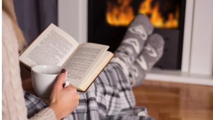 girl-in-front-of-the-fireplace-reading-book-and-warming-feet-on-fire-picture-id1060710610