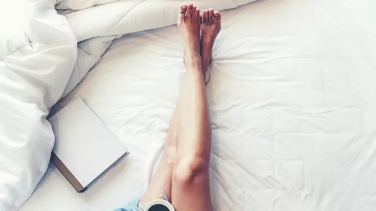 Close up legs women on white bed. Women reading book and drinking coffee in morning relax mood in winter season. Lifestyle Concept.
