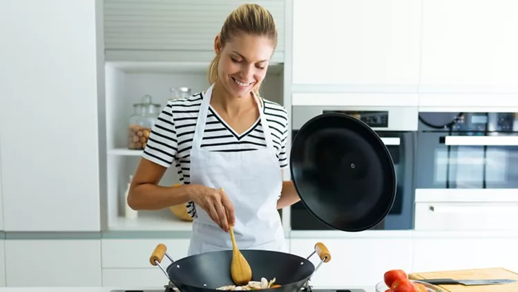 Healthy young woman cooking and mixing food in frying pan in the kitchen at home.