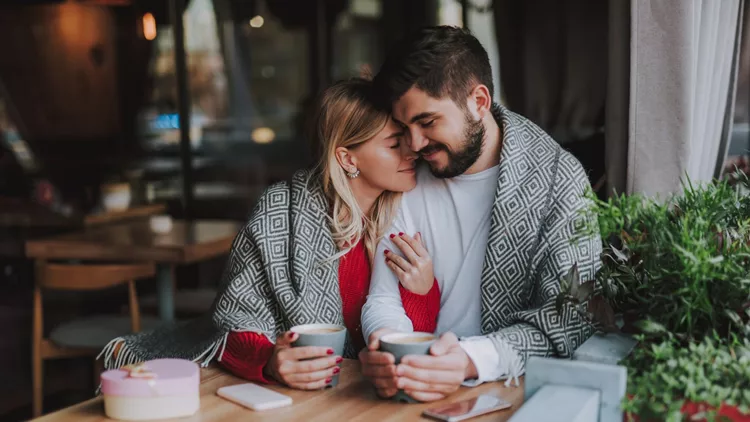 Beautiful young couple in warm blankets cuddling at cafe