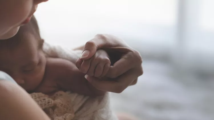 Close up Mother holding hands Asian female newborn baby and sunlight in the morning. Cute little girl three weeks old. Health, care, love, relationship concept.
