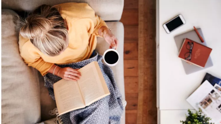 overhead-shot-looking-down-on-woman-at-home-lying-on-reading-book-and-picture-id1157317608