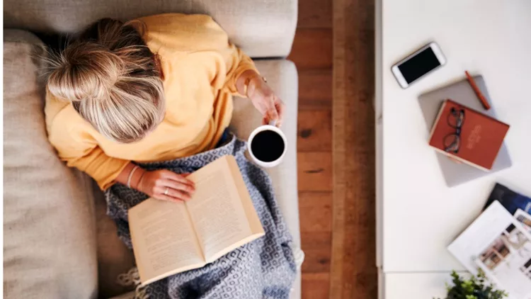 overhead-shot-looking-down-on-woman-at-home-lying-on-reading-book-and-picture-id1157317608