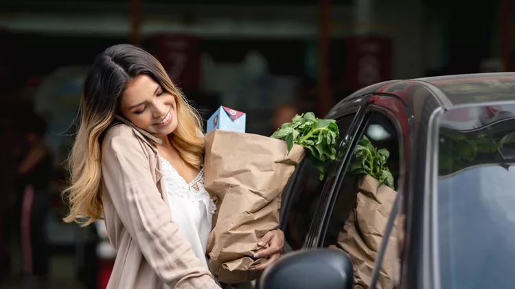 Woman multi-tasking getting in the car after shopping at the grocery store