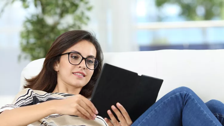 Happy woman reading an ebook on a couch at home