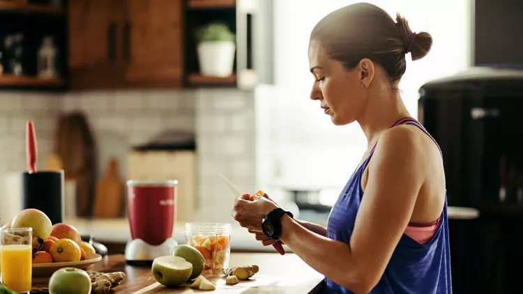 Athletic woman slicing fruit while preparing smoothie in the kitchen.