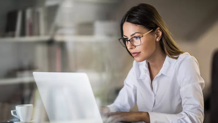 Young businesswoman typing an e-mail on laptop at home office.