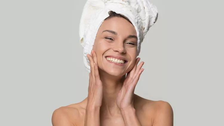Smiling woman with towel on head touch clean healthy skin