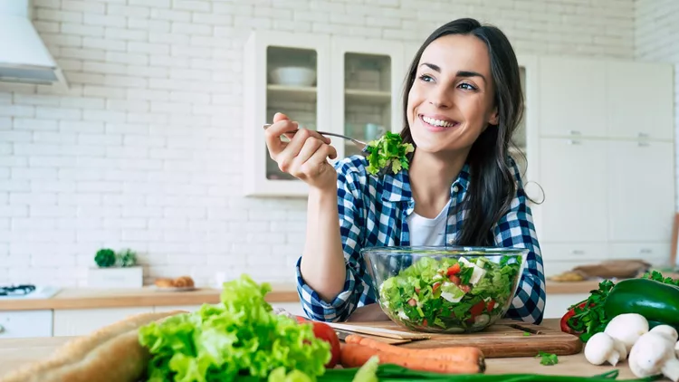 Healthy lifestyle. Good life. Organic food. Vegetables. Close up portrait of happy cute beautiful young woman while she try tasty vegan salad in the kitchen at home.
