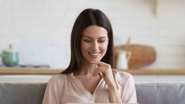 Smiling young woman using laptop, sitting on couch at home