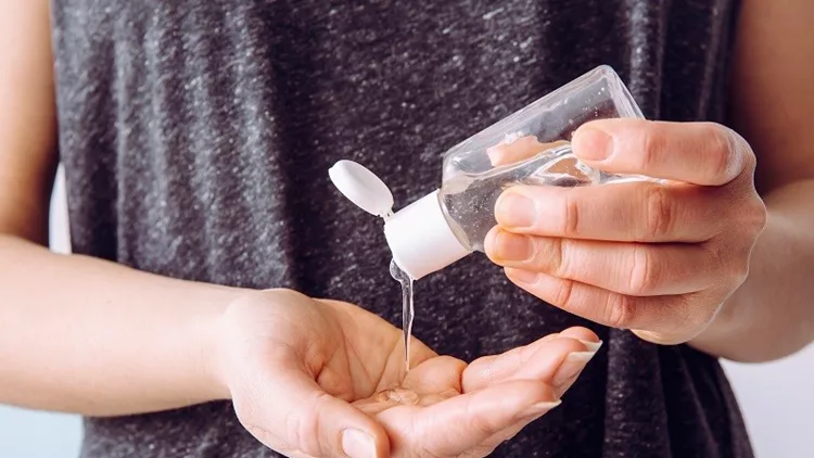 Close up view of woman person using small portable antibacterial hand sanitizer on hands.