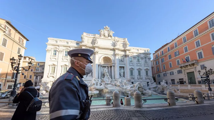 Police man wearing a face mask walks across the deserted Trevi Fountain square, Rome, Italy