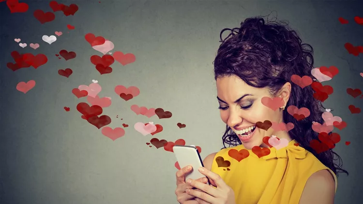 Beautiful happy woman sending love text message on mobile phone with red hearts