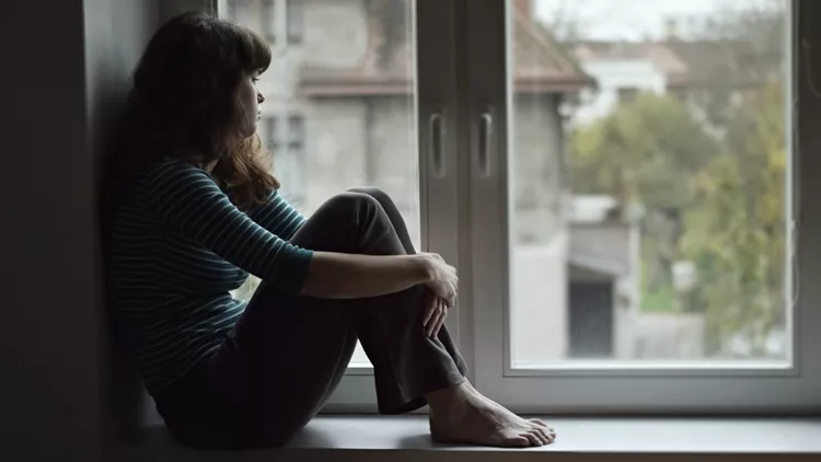 Sad young woman sitting on the window, watching out