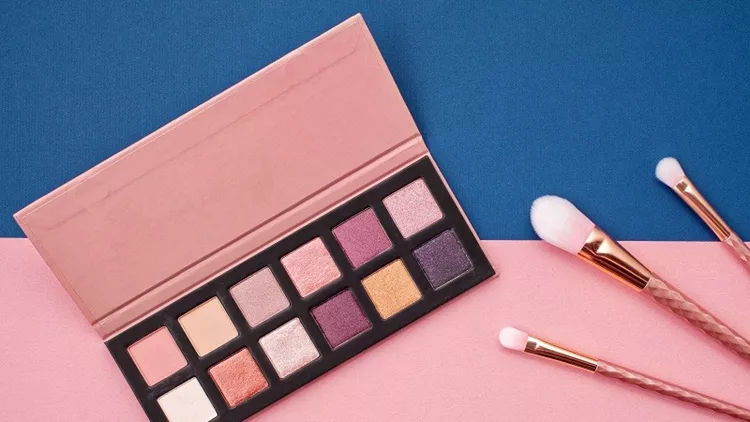 Flat lay female cosmetics collage with eye shadows and brushes on pink and blue background. Top view