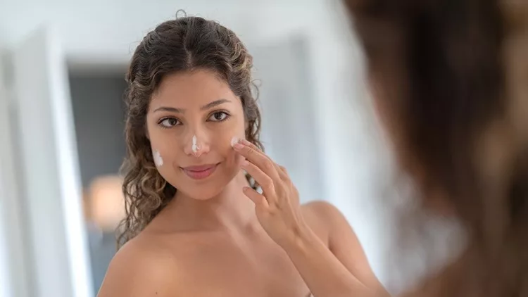 Beautiful woman applying moisturizer on her face