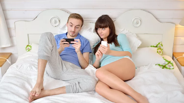Young couple together in the bed using mobile phone