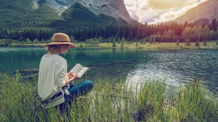 Young woman reading a book by the lake