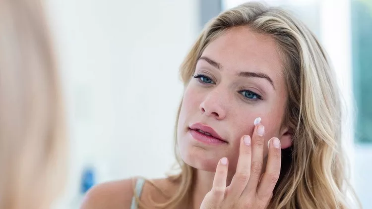 Smiling pretty woman applying cream on her face