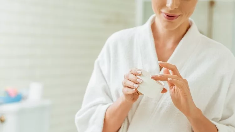 woman in bathrobe applying face cream
