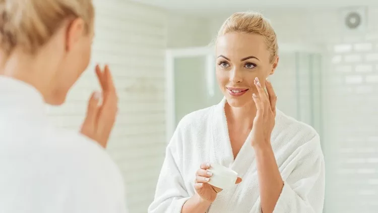 woman in bathrobe applying face cream