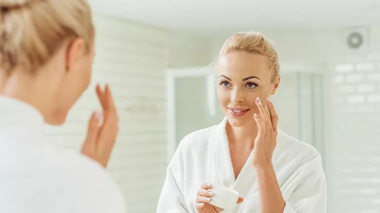 woman in bathrobe applying face cream