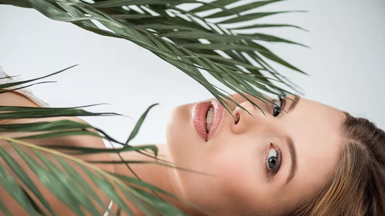 attractive young woman lying near tropical palm leaves on white