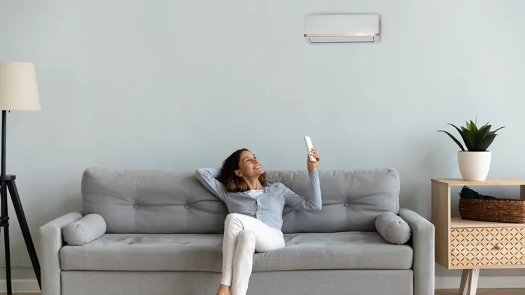 Joyful mixed race woman turning on cooler system air conditioner.