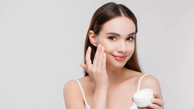 beautiful girl applying cosmetic cream on face, isolated on grey