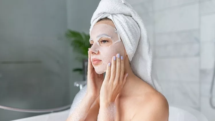 Woman  with sheet mask on face sitting in bathtub