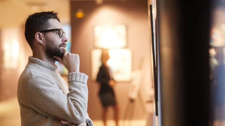 Bearded Man Looking at Paintings in Art Gallery