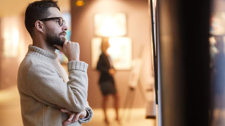 Bearded Man Looking at Paintings in Art Gallery