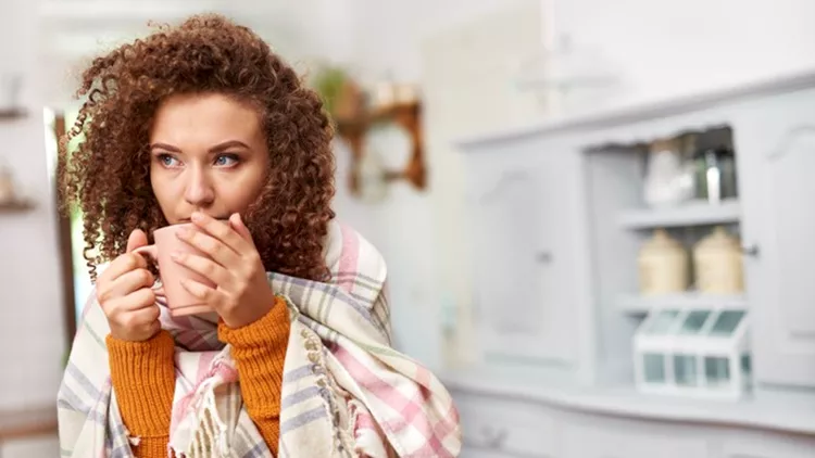 Young woman wrapped in blanket drinking hot tea
