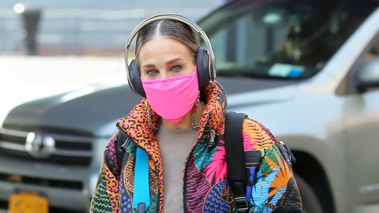 Sarah Jessica Parker Is Seen In A Colorful Coat, Matching Pink Shoes And Face Mask And Backpack Wearing Headphones As She Arrives At Her SJP Collection Shoe Sample Sale In Seaport In New York City