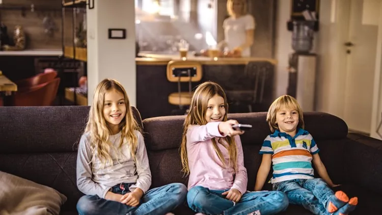 Happy kids watching TV on sofa in the living room.