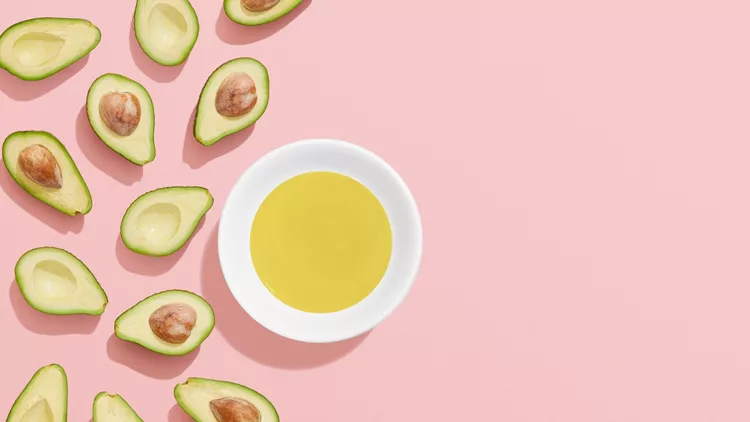 Avocado oil and halved avocados on pink background