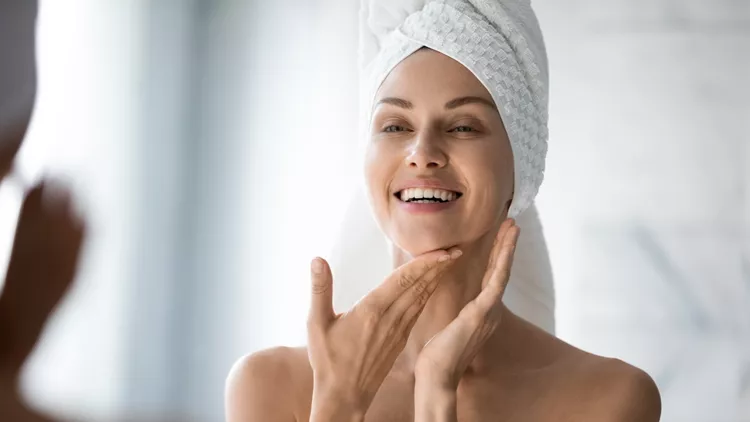 Happy lady look in bathroom mirror touching healthy face skin