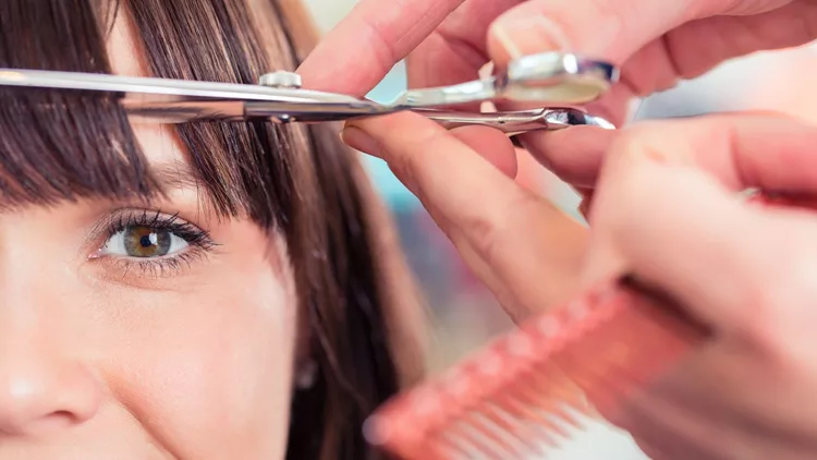 Hairdresser cutting woman bangs hair in shop