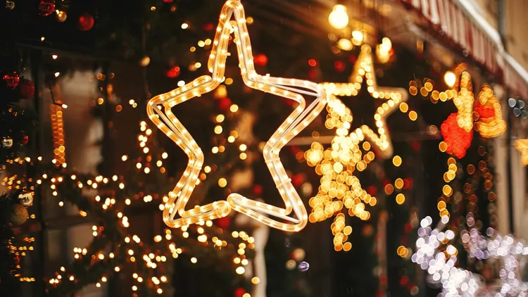 Stylish christmas golden star illumination and fir branches with red and gold baubles, golden lights bokeh on front of building at holiday market in city street. Christmas street decor