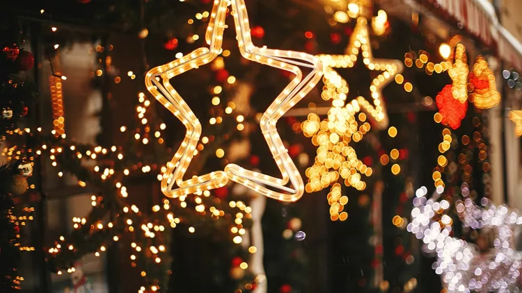 Stylish christmas golden star illumination and fir branches with red and gold baubles, golden lights bokeh on front of building at holiday market in city street. Christmas street decor