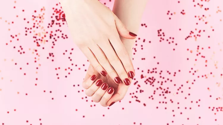 Two woman hands and falling confetti on pink background.