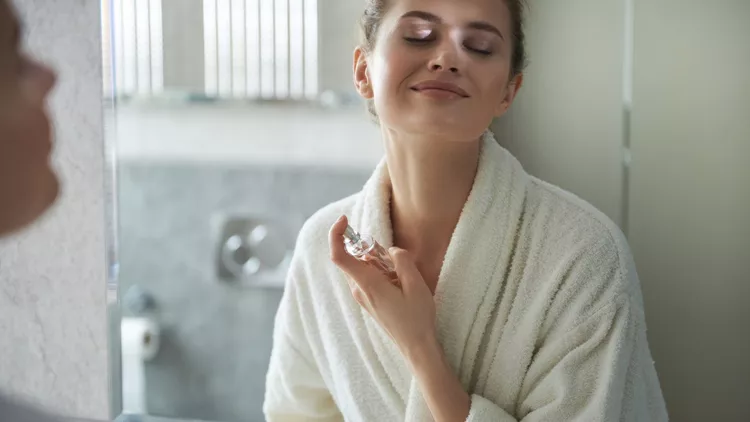 Young smiling lady enjoying her perfume in morning