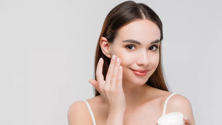 beautiful girl applying cosmetic cream on face, isolated on grey