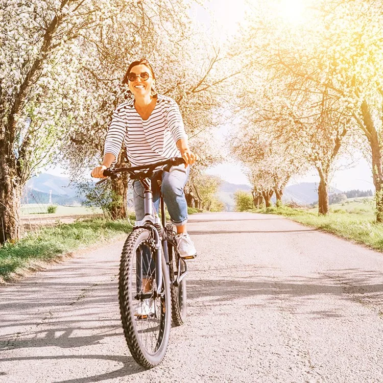 Happy smiling woman rides a bicycle on the country road under blossom trees. Spring is comming concept image.
