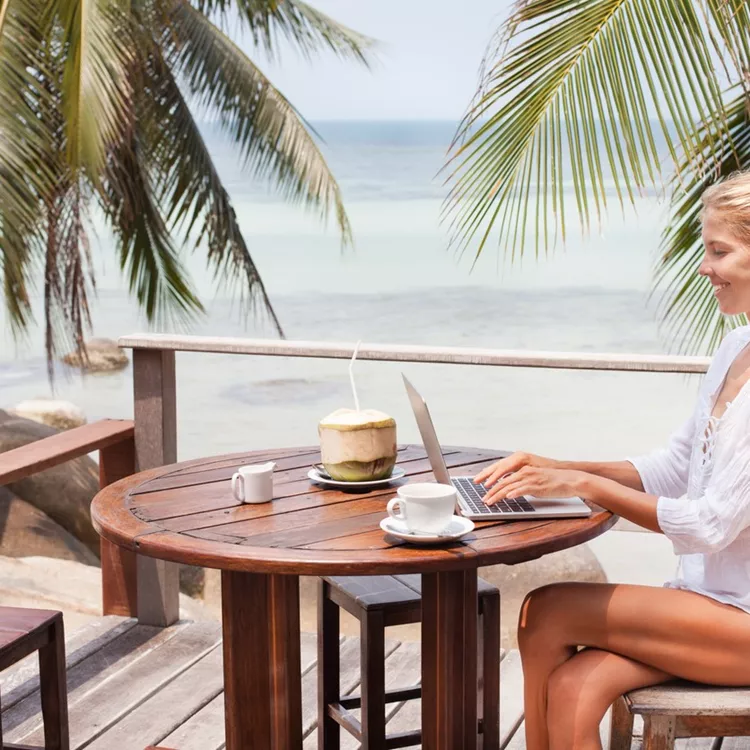 Young woman working on laptop with coffee and young coconut