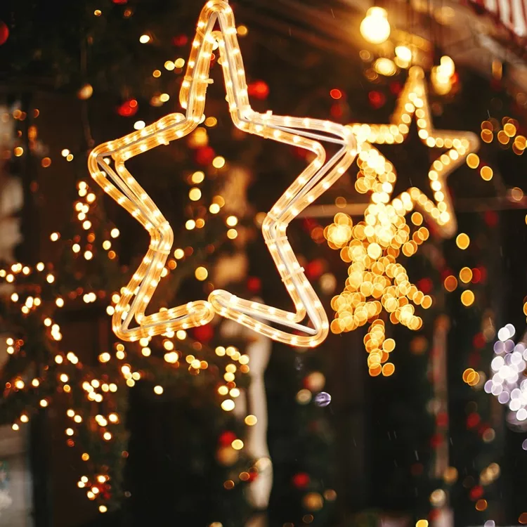 Stylish christmas golden star illumination and fir branches with red and gold baubles, golden lights bokeh on front of building at holiday market in city street. Christmas street decor